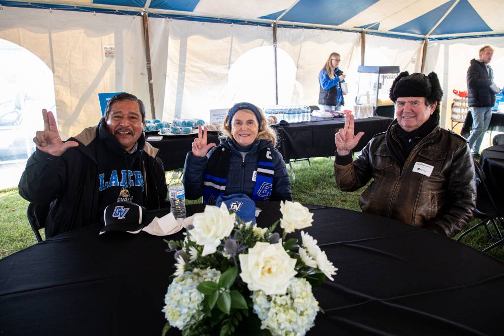 three alums sitting at a table at the tailgate.